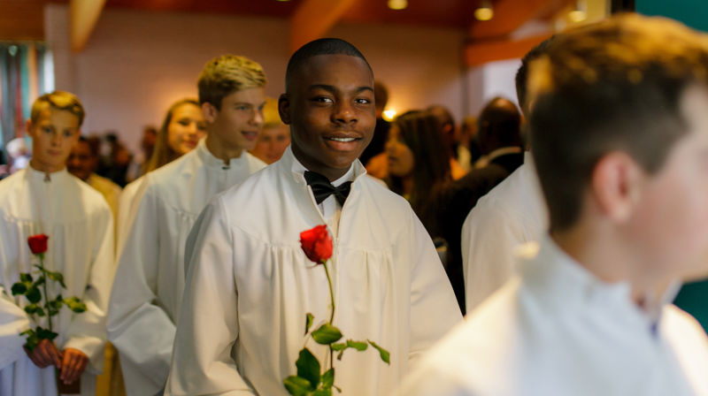 Konfirmanter går på rekke i en kirke med rose i hånda. 