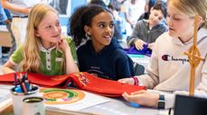 Tre jenter sitter i et klasserom og ser sammen på en stola. Foto: Den norske kirke.