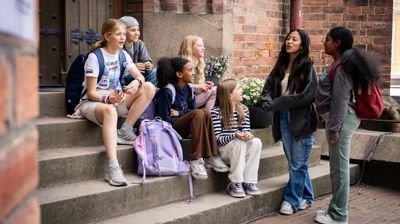 Skoleelever sitter på en kirketrapp. Foto: Den norske kirke. 