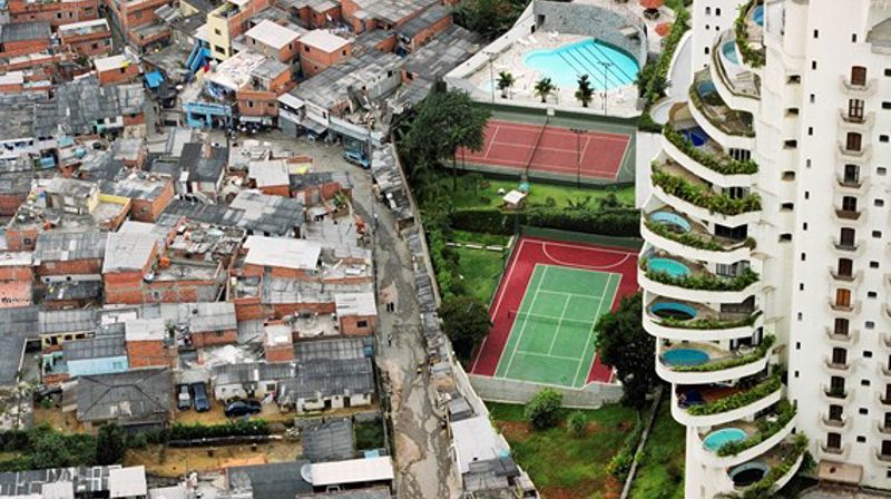 Ulikheter illustreres sjeldent godt på dette bildet, der et smalt gjerde skiller mellom slum på den ene siden og grønt gress, tennisbaner og høyhus med private basseng på hver balkong på den andre siden. (Foto: Kirkens Nødhjelp